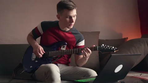 Young man learning to play electric guitar online using laptop. Stock Footage 207783535