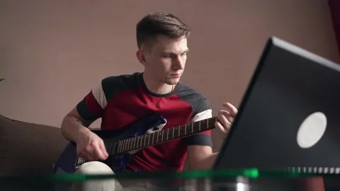 Young man learning to play electric guitar online training using laptop. Stock Footage 207783839