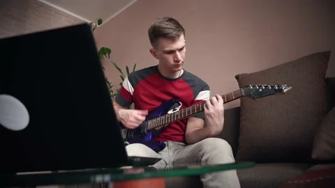 Young man learning to play electric guitar online using laptop. 動画素材 208877177