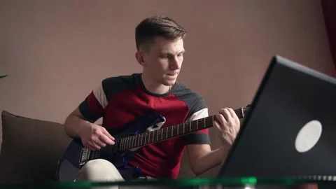 Young man learning to play electric guitar online training using laptop. Stock Footage 211812982