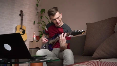 Young man learning to play electric guitar online at home Stock Footage 212612236