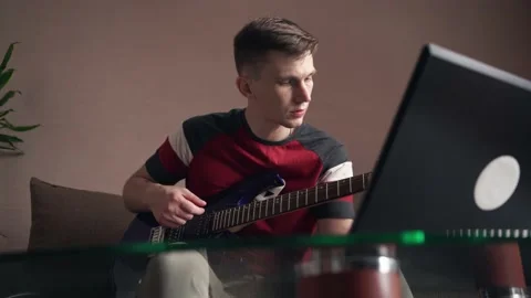 Young man learning to play electric guitar online training using laptop. Stock Footage 212612820