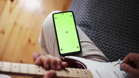 Young man is learning to play guitar by internet, green screen of phone, self Stock Footage 231007973