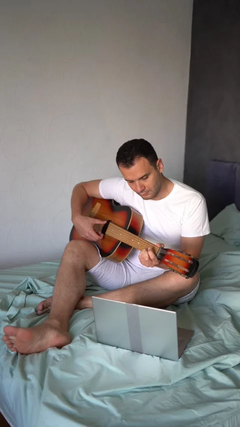 Young man is learning to play the guitar at home, a cat is lying next to hi.. Stock-Footage 276379451