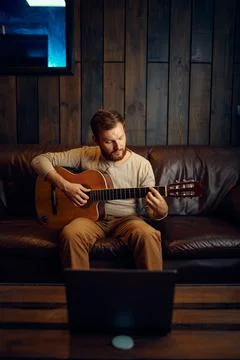 Young man learning playing guitar through internet 写真素材