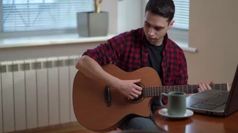 A young man learns to play the guitar using the Internet, laptop, online lesson Stock Footage 154581341