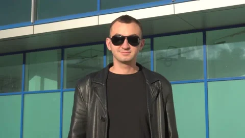 Young man in leather jacket and sunglasses standing outdoor and smiles Stock Footage 97882459