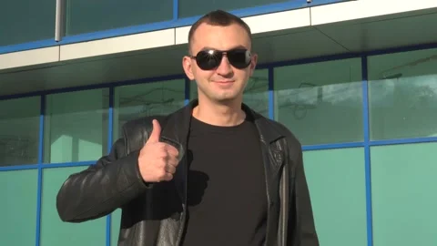 Young man in leather jacket and sunglasses standing outdoor and showing thumb up Stock Footage 97882790