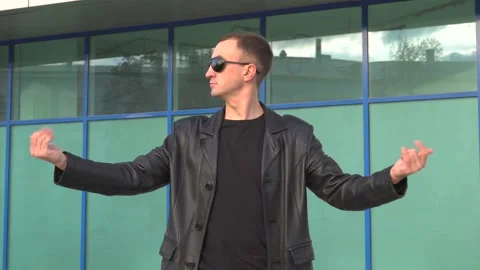 Young man in leather jacket and sunglasses standing outdoor and man inviting Stock Footage 97889939