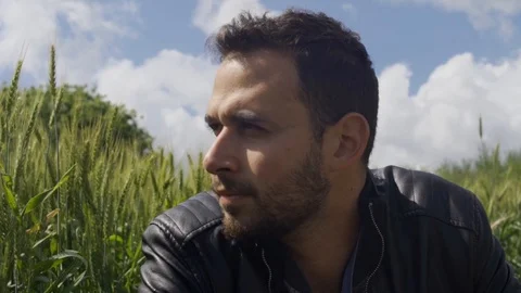 Young man with leather jacket looks over next to grain crops in countryside Stock Footage 107277304