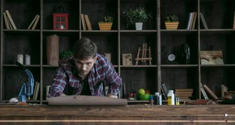 Young man leather maker looking at roll of natural leather lying on wooden table Stock Photos