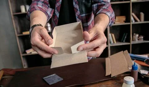 Young man leather maker manually assemble cardboard packaging box for products Stock Photos