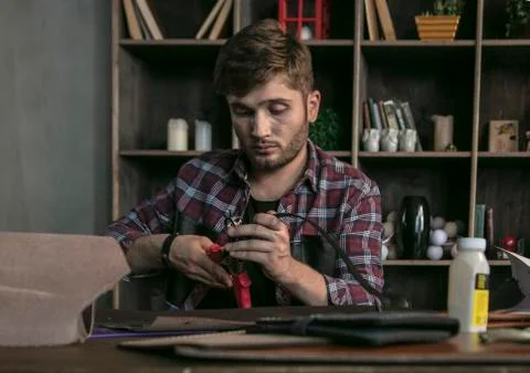 Young man leather maker sitting behind wooden table with leather templates Stock Photos