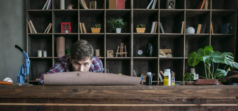 Young man leather maker working with roll leather in cozy office Stock Photos