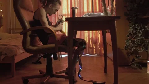 Young man with leg prosthesis and dreadlocks works at table 库存影片 194600350
