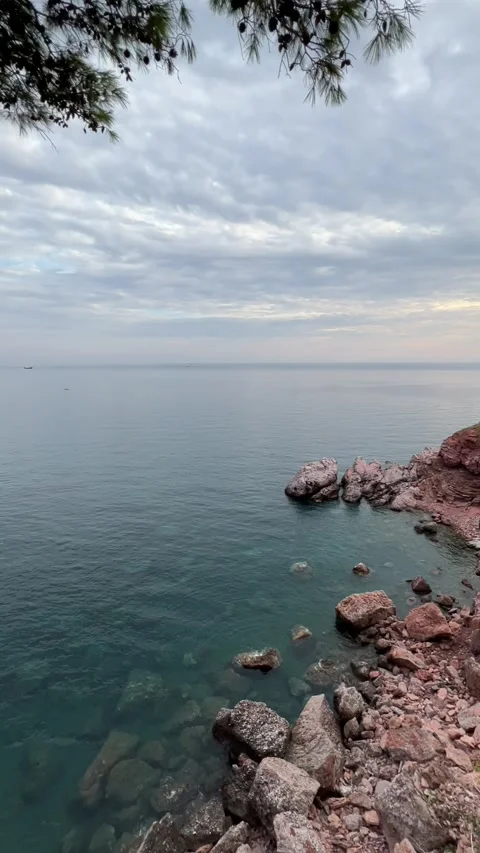 A young man, legs dangling, is sitting on a rock overlooking the bay Stock Footage 251008517