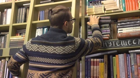 A young man in the library climbed the stairs and looks for a book on the booksh Stock Footage