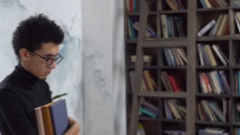 Young man in library holding books looking camera unhappy Stock Footage 121646878
