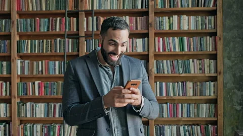 Young Man In The Library With Mobile Phone In His Hands. Stock Footage 140223086