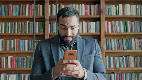 Young Man In The Library With Mobile Phone In His Hands. Vídeos de archivo 140223485
