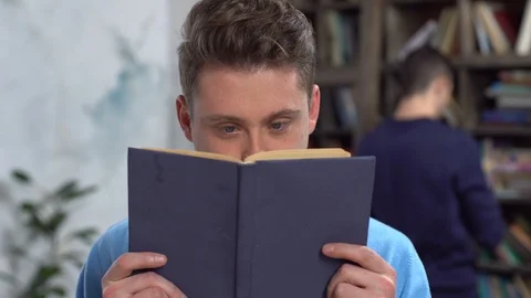 Young man in library reading book looking camera playful Stock Footage 121539421