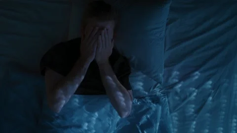 A young man lies awake in bed at night, turning restlessly due to insomnia Stock Footage 314023615