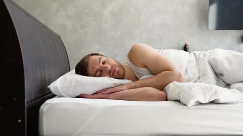 Young man lies down in bed under the covers and falls asleep at home, relaxation Video stock 242130908