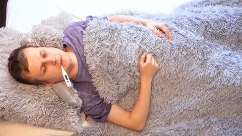 A young man lies under a blanket in bed with discomfort. Check the temperature o Video stock 98923596