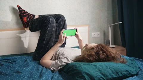 A young man lies upside down in bed and does something on the phone Stock-Footage 196812481