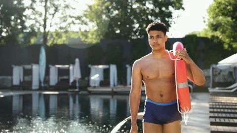 Young man lifeguard protecting pool area, carrying a rescue buoy on summer Stock Footage 333564992