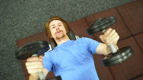 Young man lifts dumbbells while lying.man in a blue t-shirt is raises in gym Vidéo 163460413