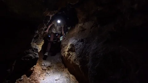 Young man with light on forehead is exploring the dark cave. Primorye, Russia Stock Footage 104702957
