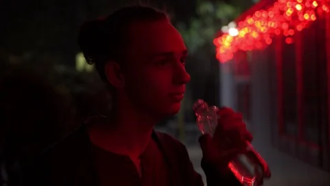 Young man lighted of red light drinks water outdoors at night 3 動画素材 95862122