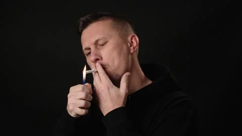 Young man lighting a cigarette over black background Video stock 262634442