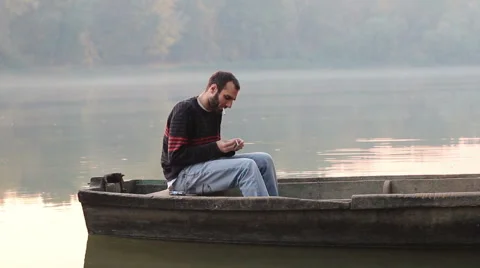 Young man lighting a cigarette on a small river boat Stock Footage 51100850