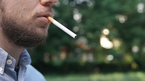 Young man lights a cigarette close-up outdoors in a park 스톡 동영상 130006378