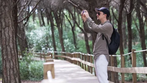 Young man in linen clothes taking photo on phone while walking through forest Stock Footage 310685126