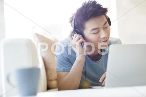Young Man Listening To Music With Laptop On The Sofa
