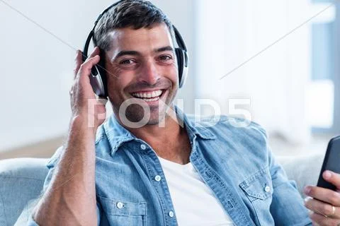 Young Man Listening To Music While Using Mobile Phone