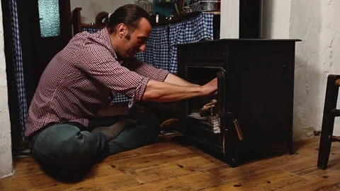 Young man loading dry logs inside a vintage wooden burning stove, heating house Stock Footage 266822067