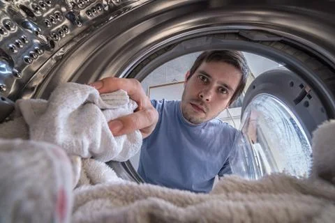 Young man is loading laundry in washing machine. View from inside. Stock Photos