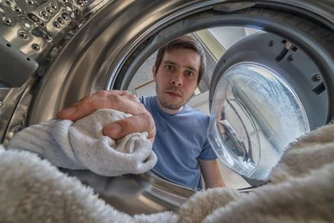 Young man is loading laundry in washing machine. View from inside. Stock Photos