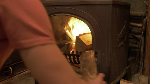 Young man loading up stove with birch logs stokes embers closes door Stock Footage 141748393