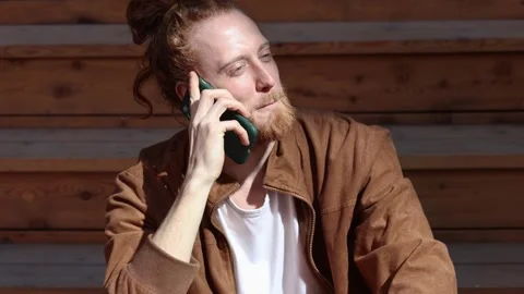Young man with long, curly red hair and a beard, chatting on his smartphone. Stock Footage 252736963