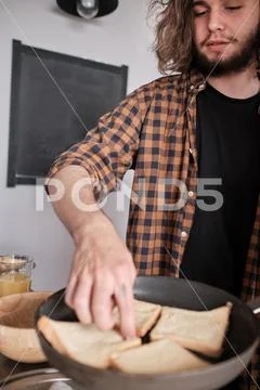 Young man with long hair cooks something in the kitchen. Stock Photos