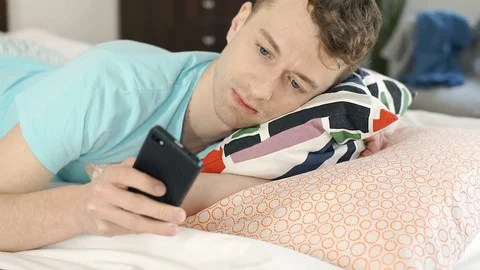 Young man look happy while lying in bed and using smartphone, steadycam shot Stock-Footage 76527999