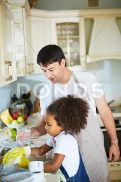 Young man looking after his daughter washing dishes Stock Photos