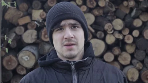 Young Man Looking Anxious and Sad into the Camera with Wooden Logs in Background Video stock 239654517