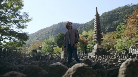 Young man looking around and walking past Buddhist statues and stone statues nea Stock Footage 199461837