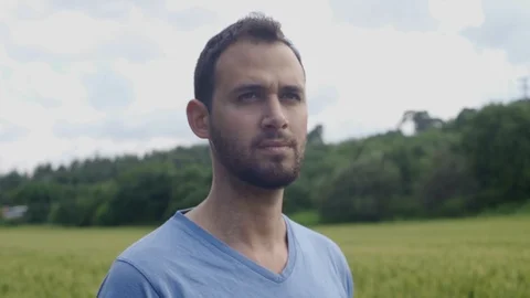 Young man looking around as camera moves. Set in countryside fields Stock Footage 107263172